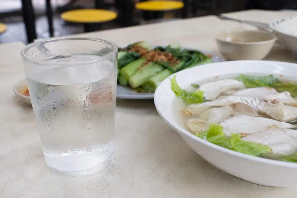A glass of water beside sliced fish soup at a hawker table